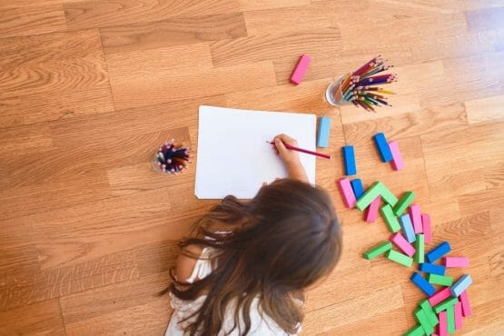 Adorable toddler lying down on the floor drawing using paper and pencils at kindergarten Adorable toddler lying down on the floor drawing using paper and pencils at kindergarten